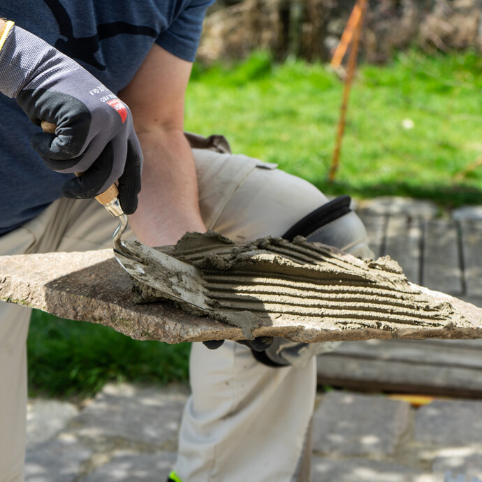 Steinkleber mit Zahnkelle auf die Rückseite der Polygonalplatten aus Porphyr auftragen.