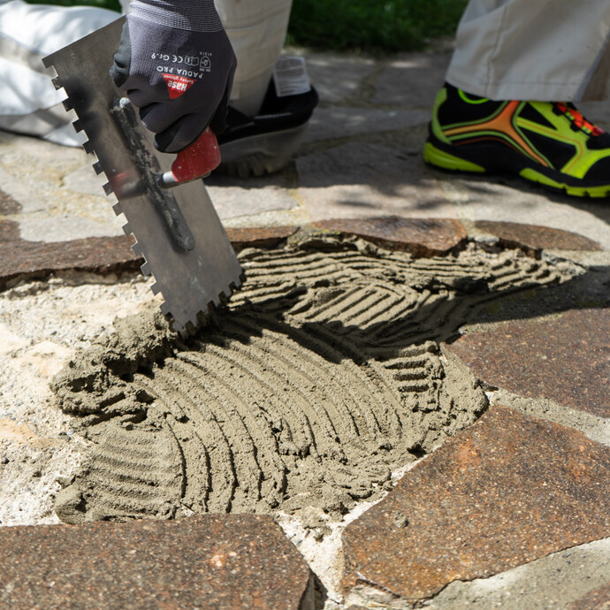 Steinkleber auf den Unterbeton mit Zahnkelle auftragen für die Verlegung von Terrassenplatten