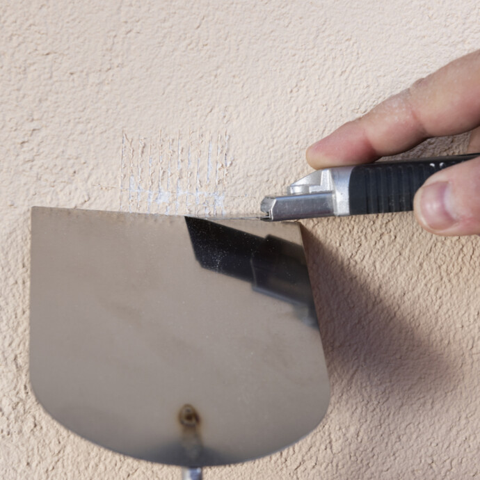 Waagerechte Schnitte mit dem Cuttermesser in den Altanstrich zur Putzgrundprüfung setzen